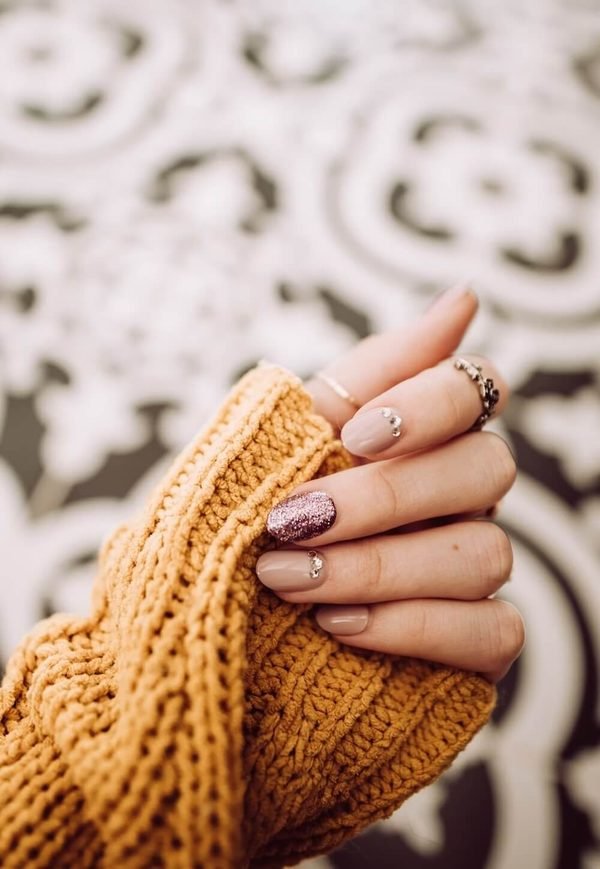 A finished manicure in soft nude with glitter and crystal detail
